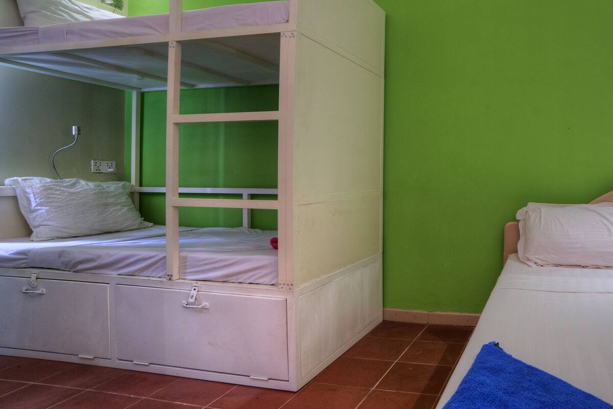 A room with bunk beds and a single bed, green walls, and a tiled floor.
