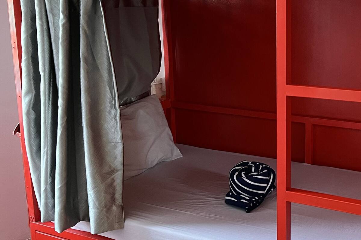 A red bunk bed with a single mattress and a striped bag on it.