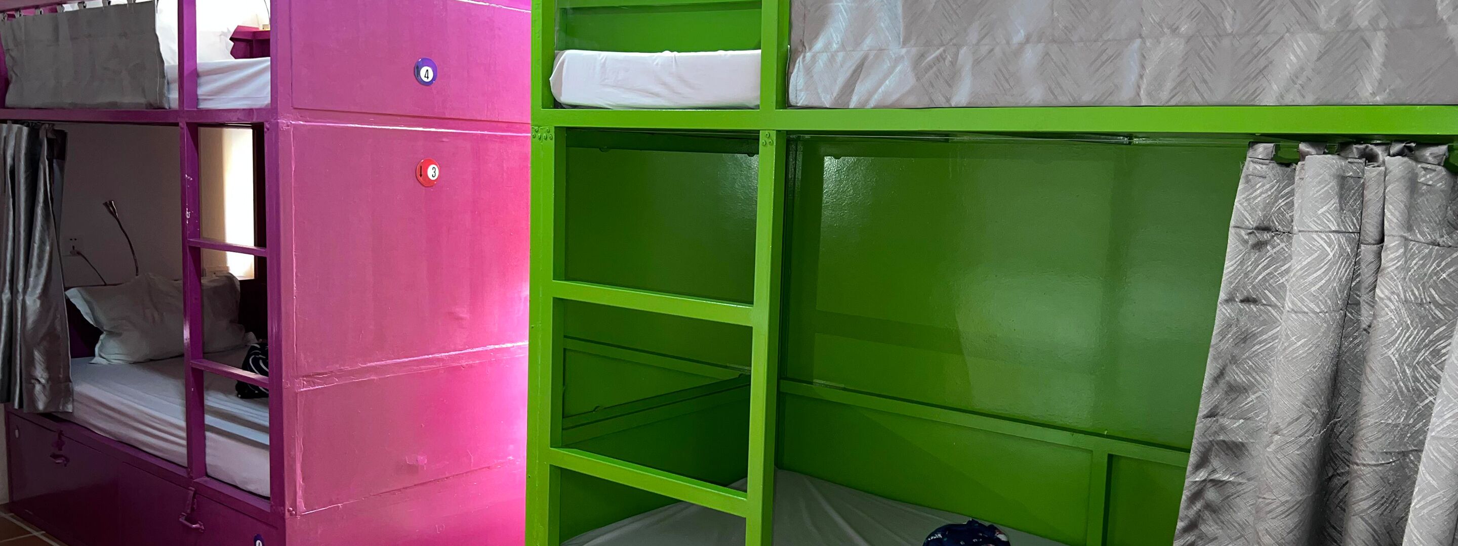 A bunk bed room with a pink and green color scheme, featuring a bunk bed on the left and a single bed on the right.