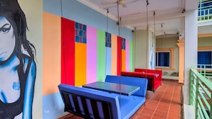 A hotel room with a colorful wall mural, a bed with a blue headboard, and a red bench. - The Funky Village (Siem Reap)