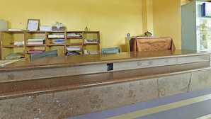 Un mostrador de recepción con encimera de mármol marrón, estanterías de madera con diversos objetos y una pared amarilla.