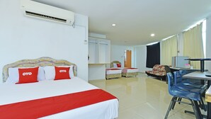 Una habitación de hotel con una cama grande, dos camas más pequeñas, un escritorio con sillas y un equipo de aire acondicionado.