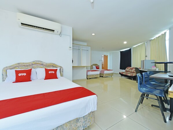 Una habitación de hotel con una cama grande, dos camas más pequeñas, un escritorio con sillas y un equipo de aire acondicionado.