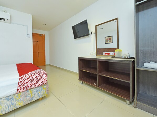 Una habitación de hotel con cama, televisor montado en la pared, aparador de madera y espejo.