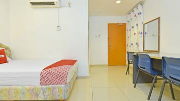 A hotel room with a bed, an air conditioning unit, a desk with chairs, and a door.