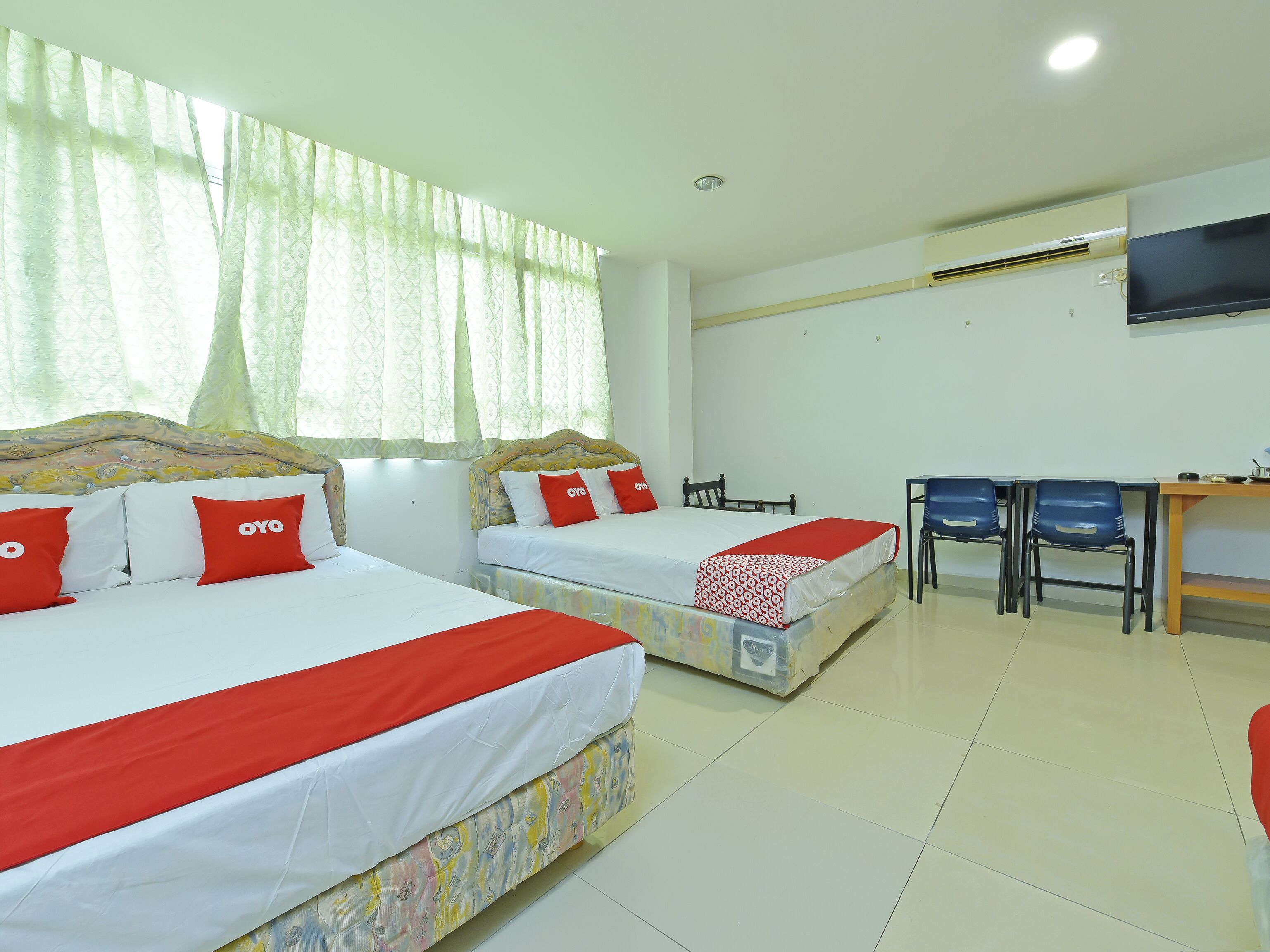 A hotel room with two beds, a desk, chairs, and an air conditioning unit.
