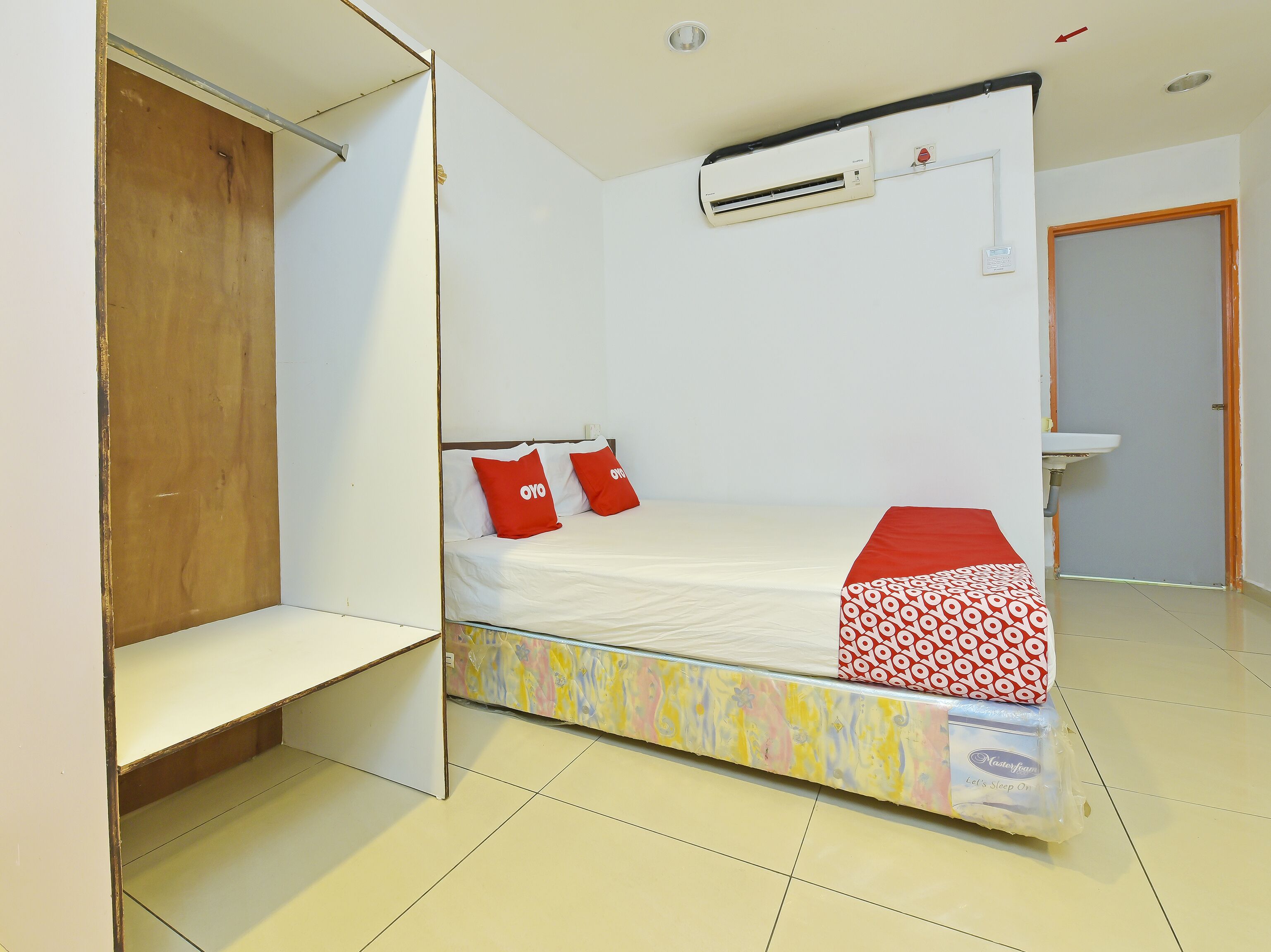 A compact room with a bed, a wardrobe, a bathroom, and an air conditioning unit.