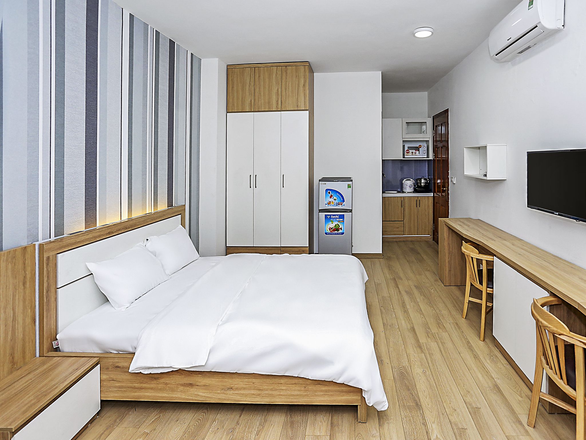 A hotel room with a bed, a desk, a kitchenette, and a TV.