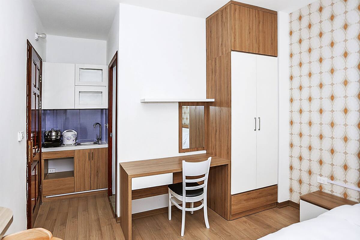 A compact room with a wooden desk, a chair, a bed, and a wardrobe.