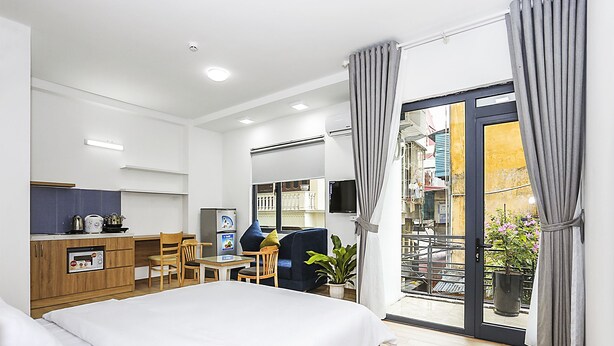Une chambre d’hôtel moderne équipée d’un lit, d’une kitchenette, d’un coin repas et d’un balcon avec des rideaux.