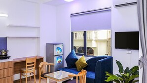 Un espace de vie compact comprenant un canapé, des fauteuils, une petite table, un réfrigérateur, un téléviseur et une plante en pot.