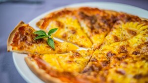 Ananas- ja kinkkusiivut päällysteellä varustettu pizza valkoisella lautasella.