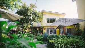 A courtyard with a yellow building, outdoor seating, and greenery. - Suan Tung Coffee (Chiang Rai)
