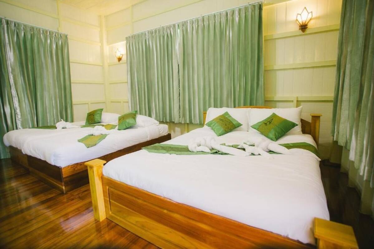 Two wooden beds with white linens and green pillows, in a room with green curtains and wall sconces.