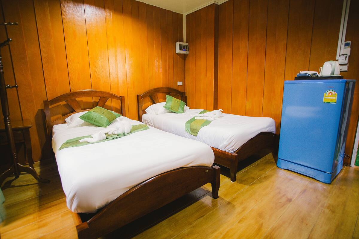 Two wooden beds with white linens and green pillows in a room with wooden walls and a blue refrigerator.