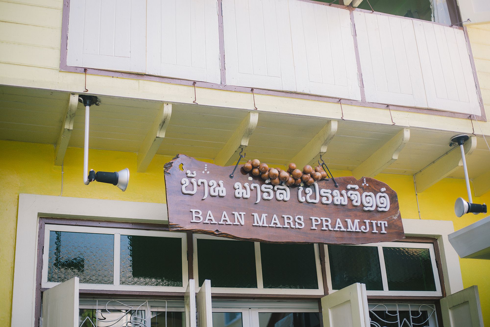 A building with a sign that reads "BAAN MARS PRAMJIT" and a bell hanging from the roof.