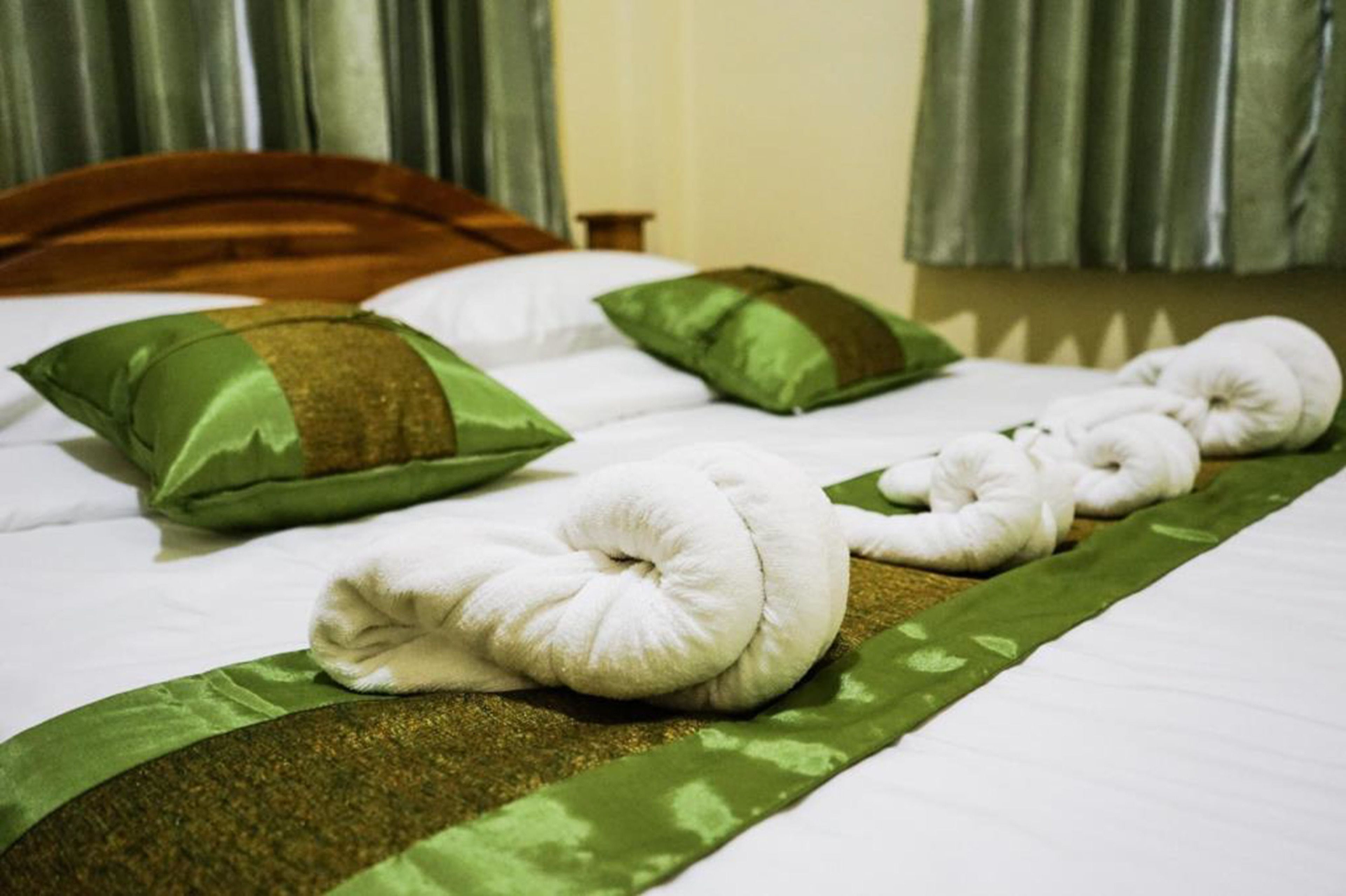 Un letto ben rifatto con cuscini verdi e bianchi, una coperta verde e oro, e asciugamani bianchi disposti in fila.