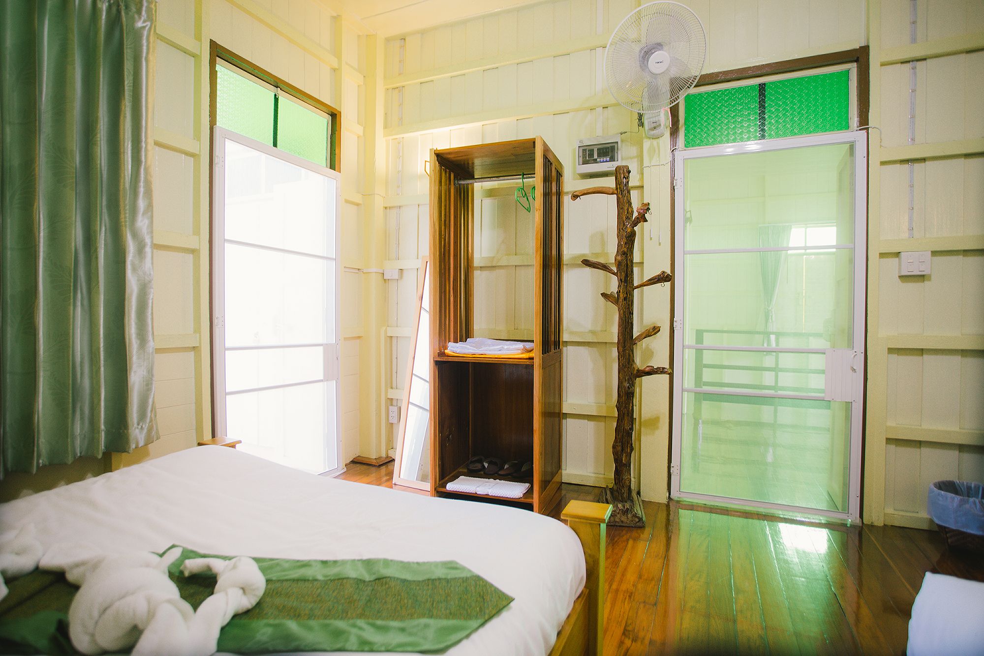 Quarto de hotel com uma cama, guarda-roupa de madeira, um ventilador e uma porta de correr.