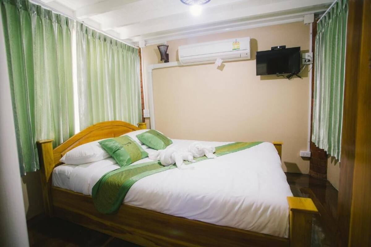 A neatly made bed with white and green bedding, a wooden headboard, and a green curtain on one side.