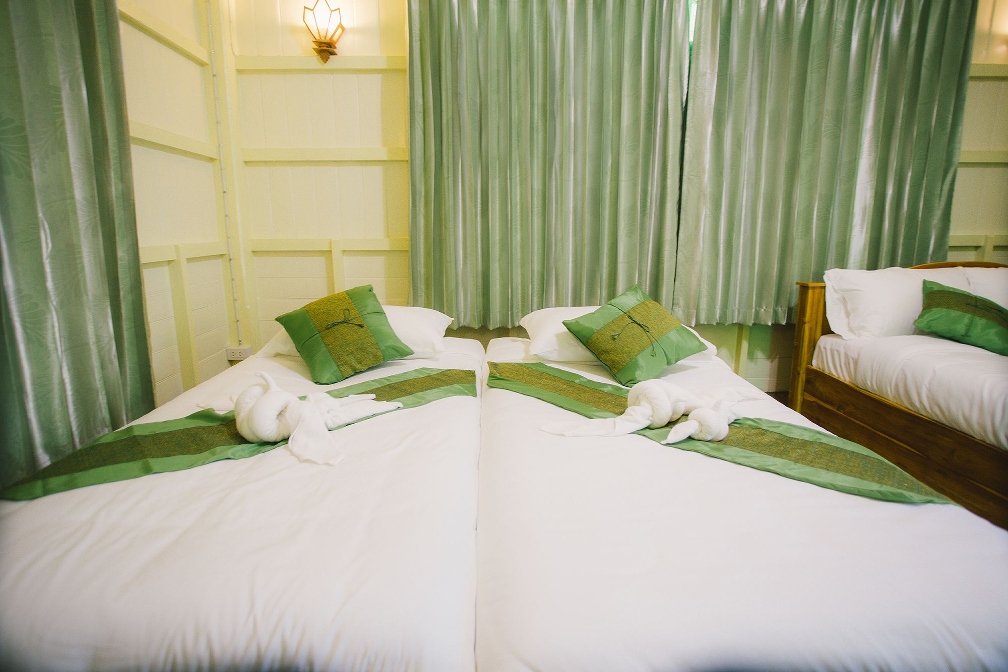 A hotel room with two beds, each with white bedding and green accents, and a wooden headboard.
