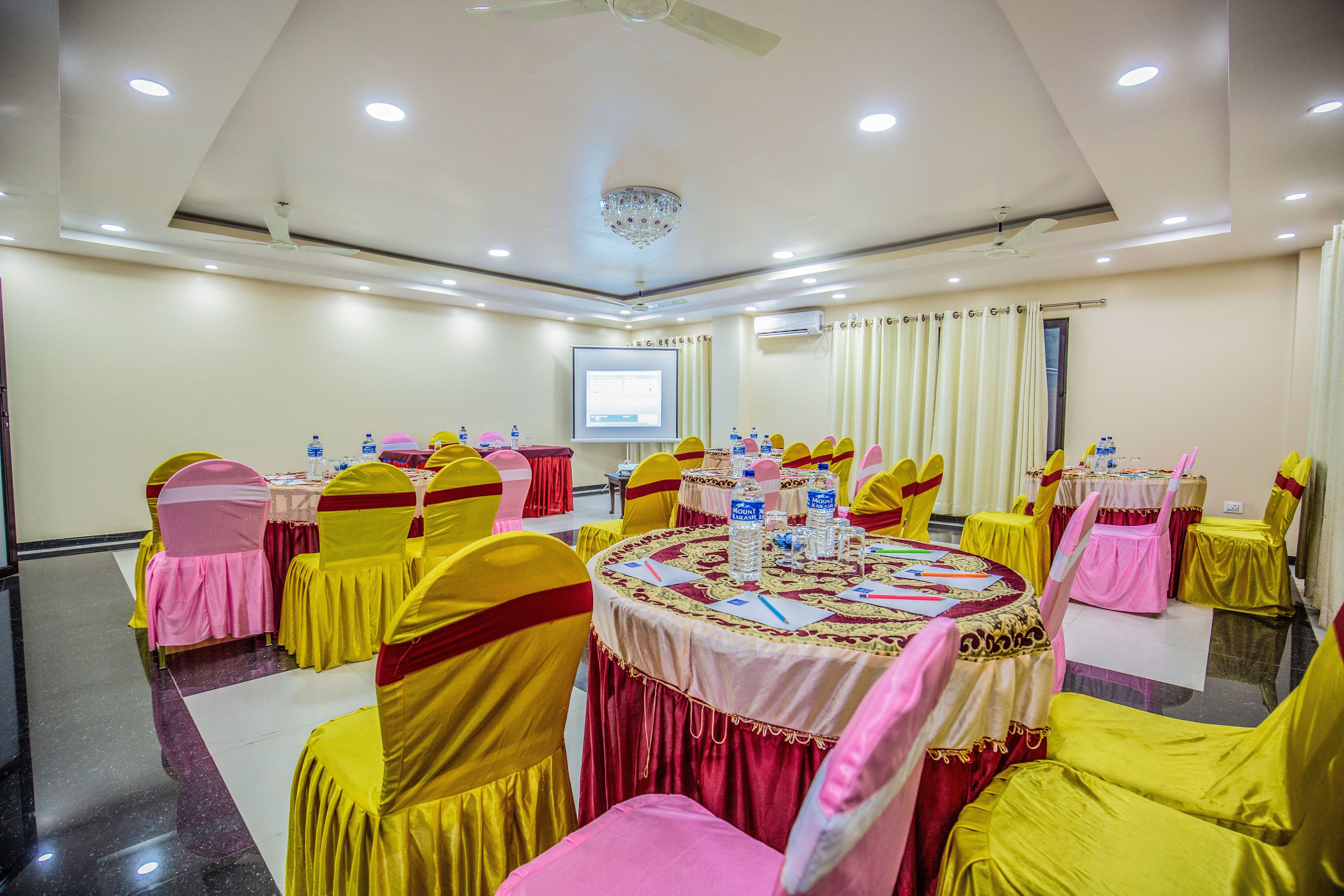 A conference room with round tables, yellow chairs, and a projector screen.