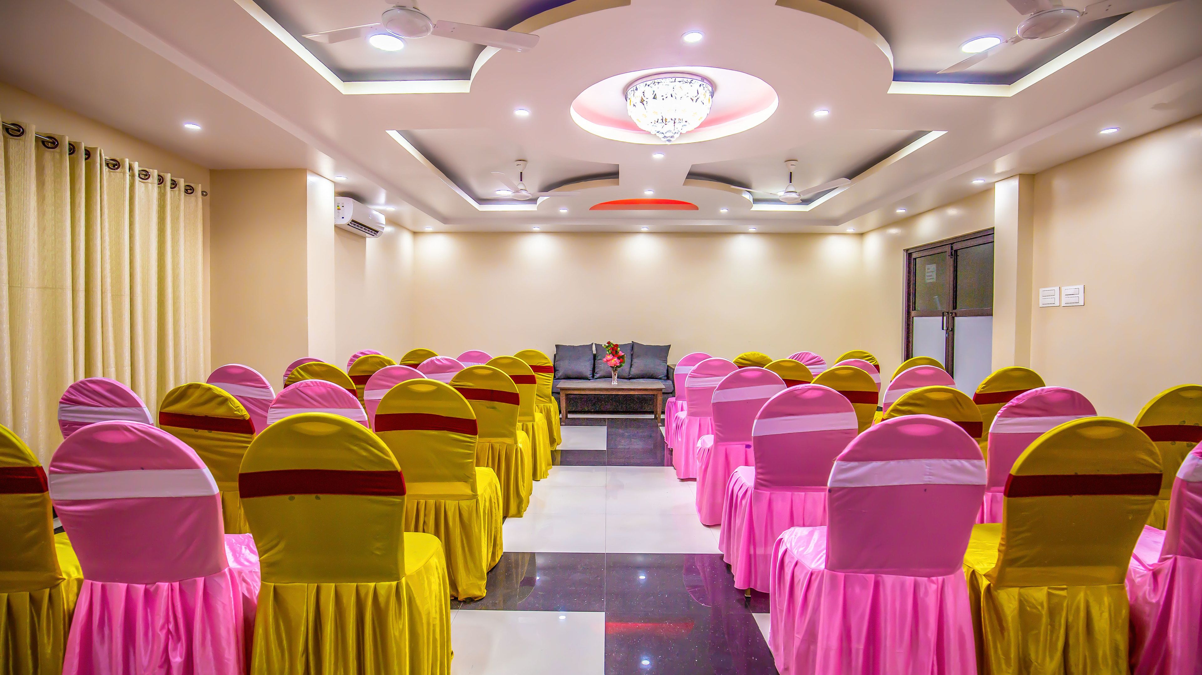 Une salle de conférence avec des rangées de chaises, un canapé et un lustre.