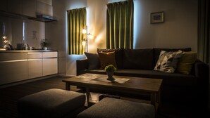 Una sala de estar moderna con un sofá, una mesa de centro con una planta, y un área de cocina con armarios y una estufa.