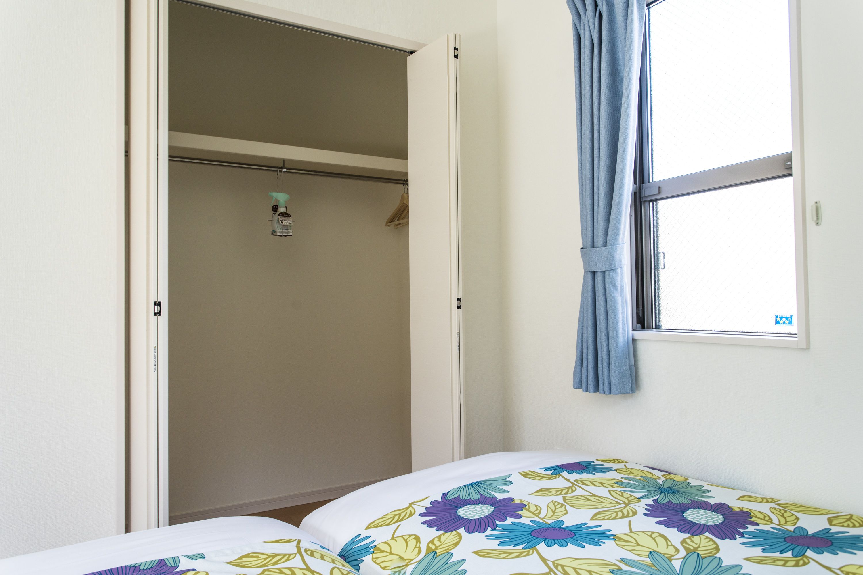 A bedroom with a bed, a window with a curtain, and a closet with a hanging rack.