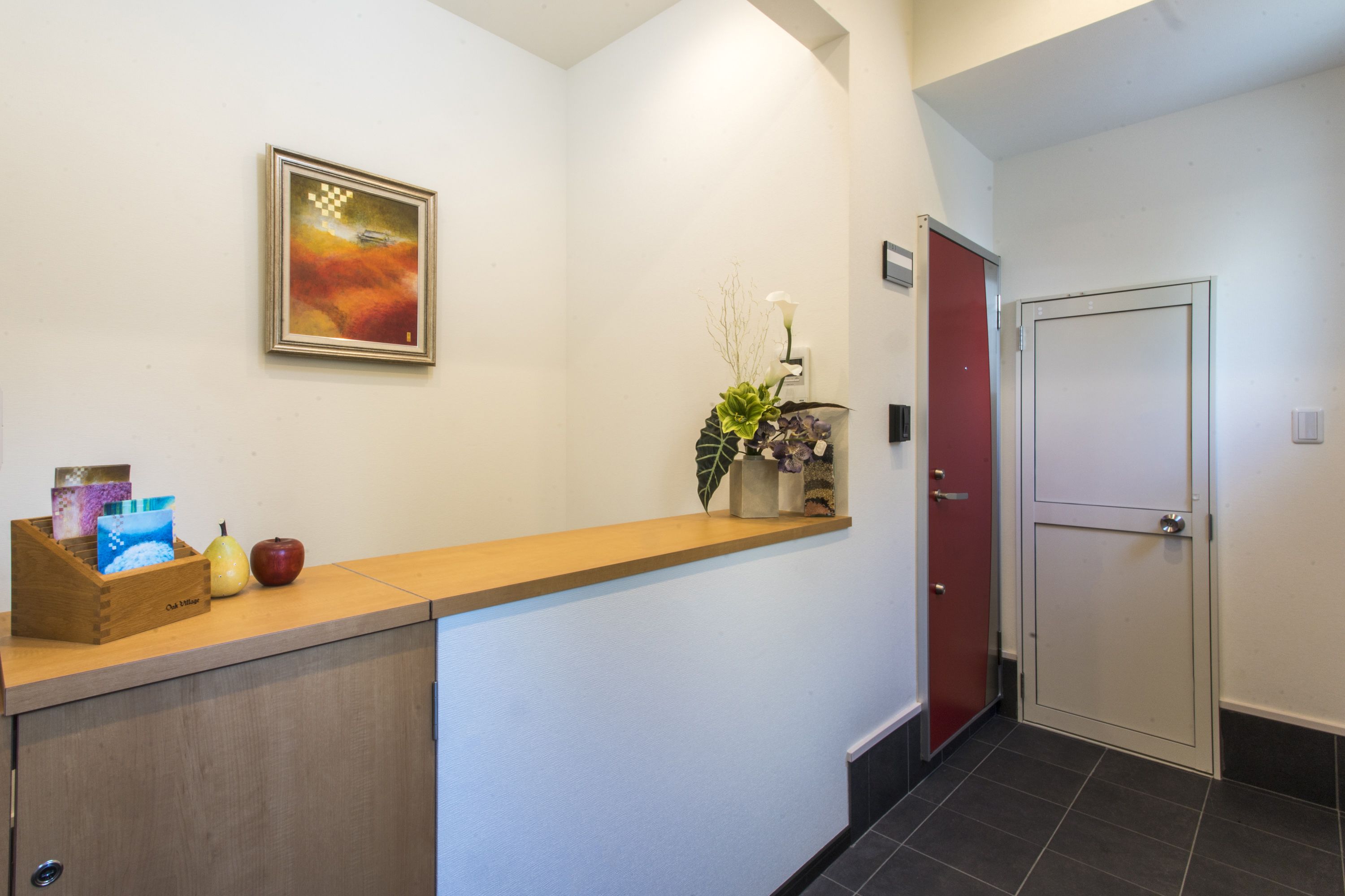 A reception area with a wooden counter, a framed artwork, a vase with flowers, and a red door.
