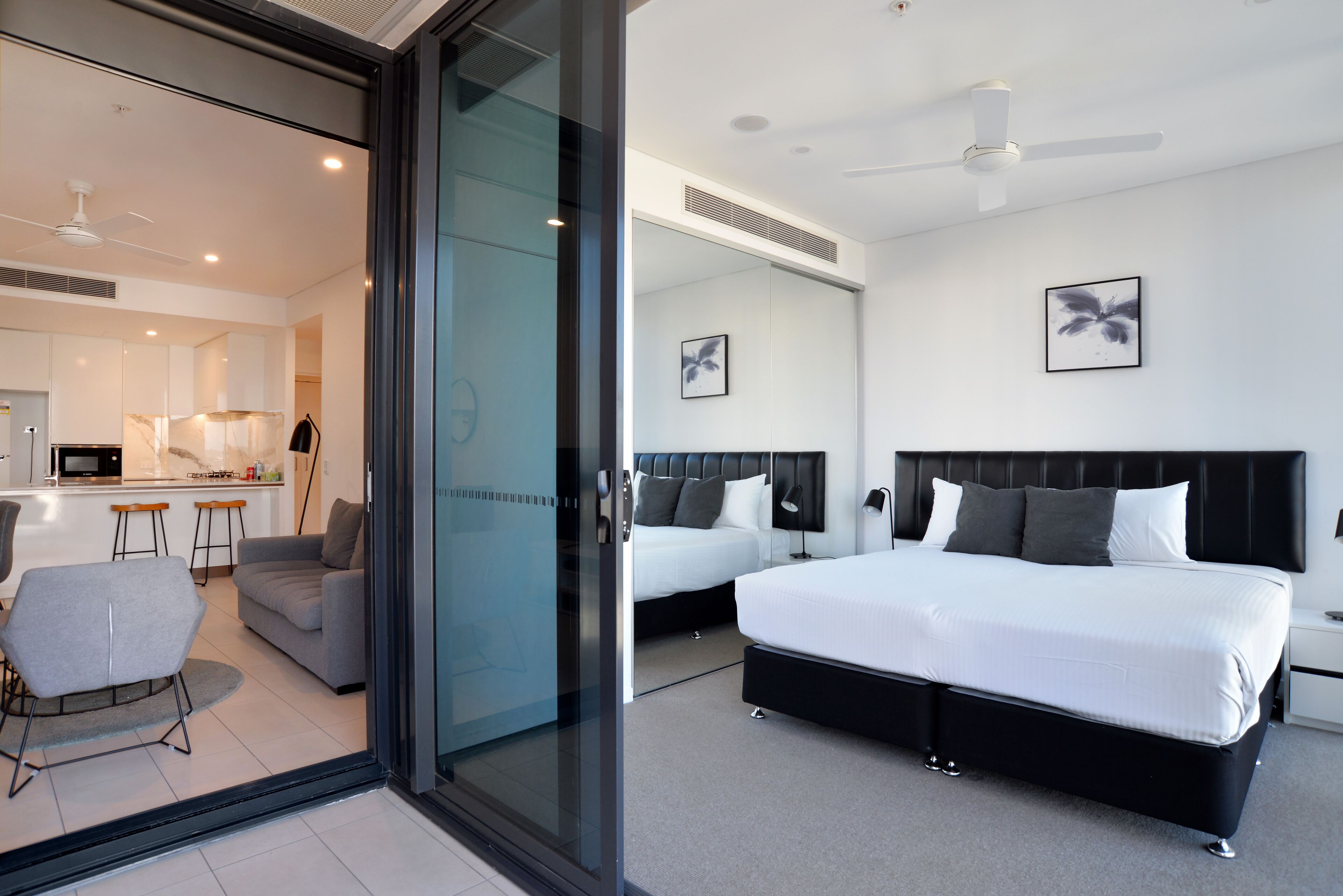 Ein modernes Hotelzimmer mit einem großen Bett, einer separaten Sitzecke mit Sofa und Sesseln, einer Küchenzeile und einer Glasglastür, die auf einen Balkon führt.