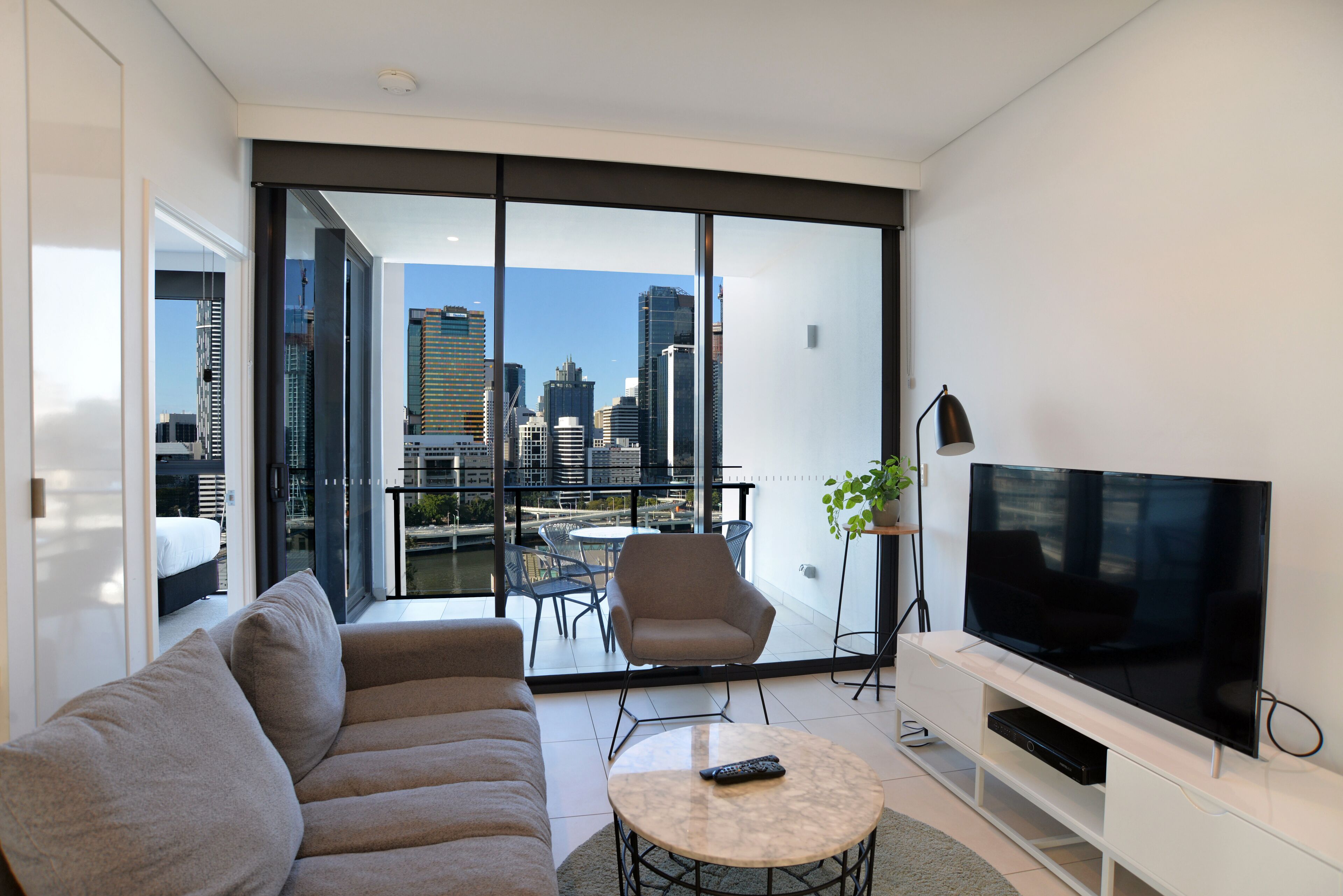 A modern living room with a sofa, a coffee table, a TV, and a balcony with a city view.