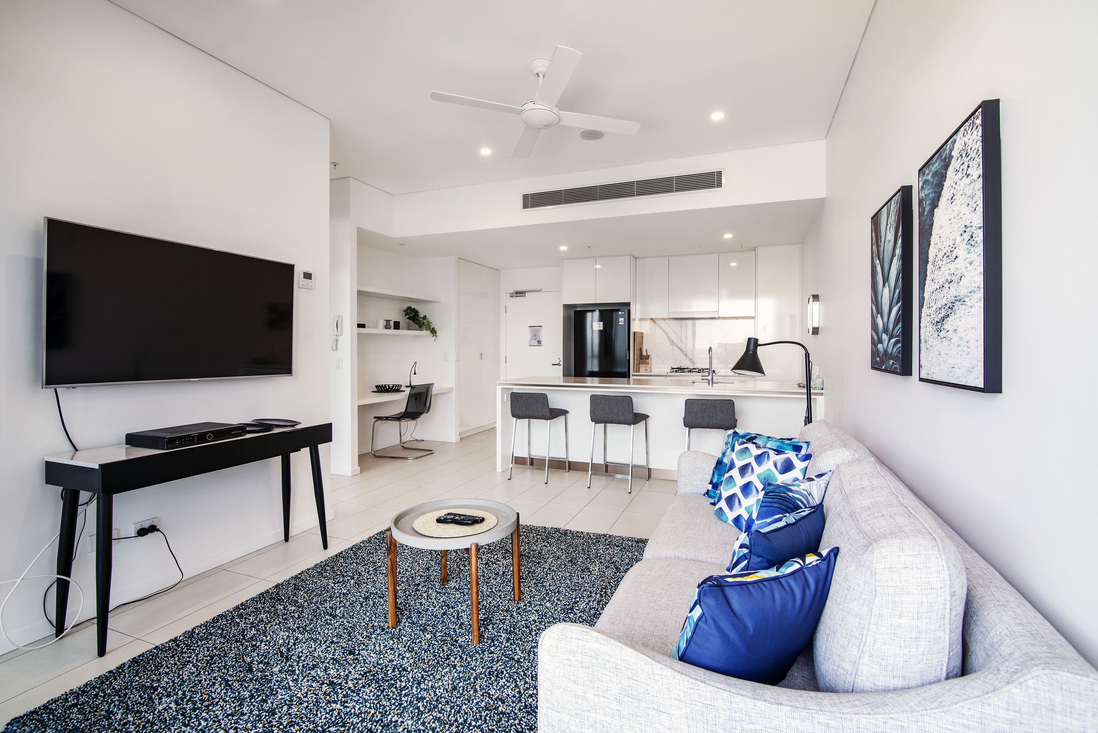 Un salon moderne avec un téléviseur à écran plat, une table basse noire et un canapé gris agrémenté de coussins bleus.