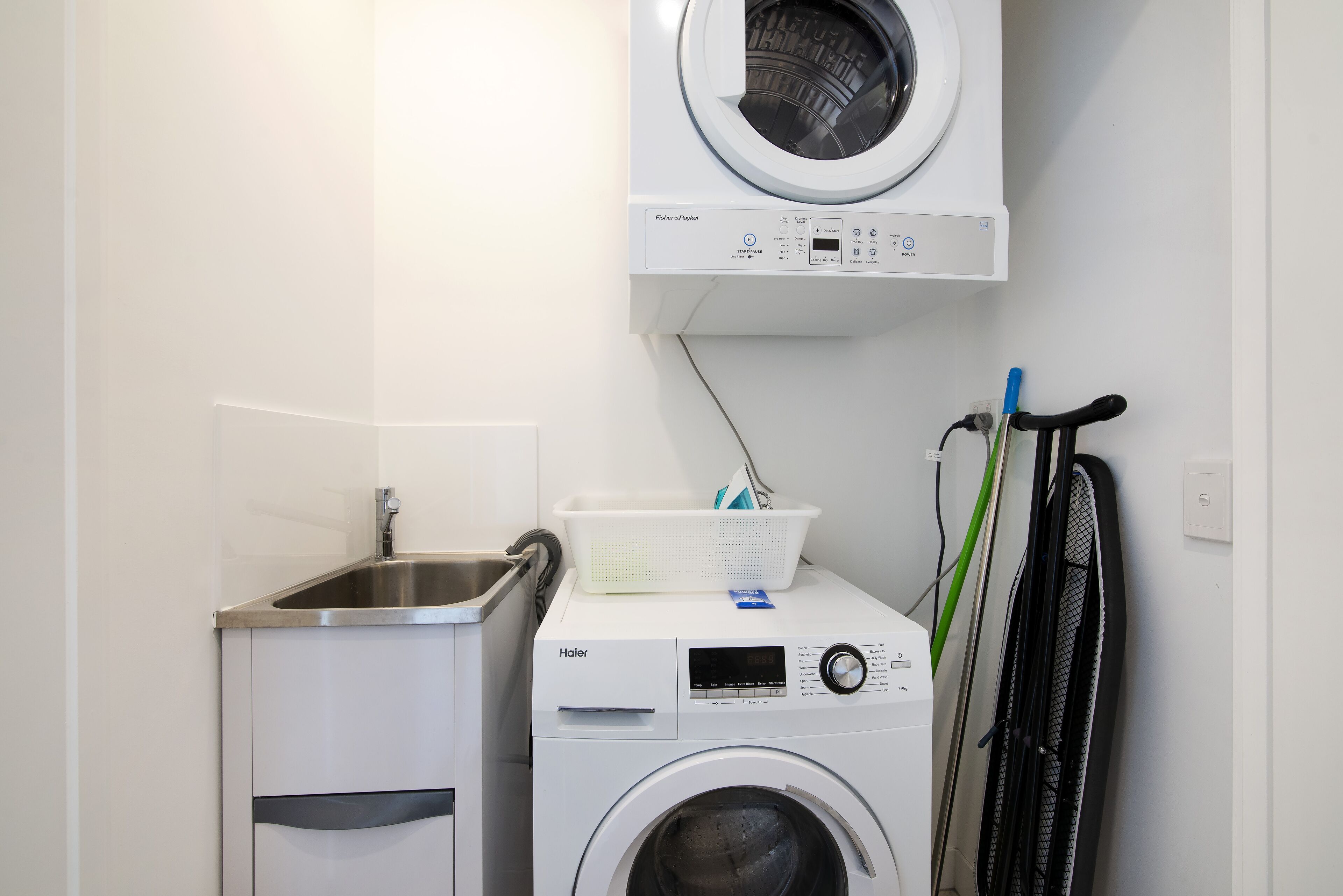 A compact laundry area with a front-loading washer and dryer, a sink, and a bicycle rack.