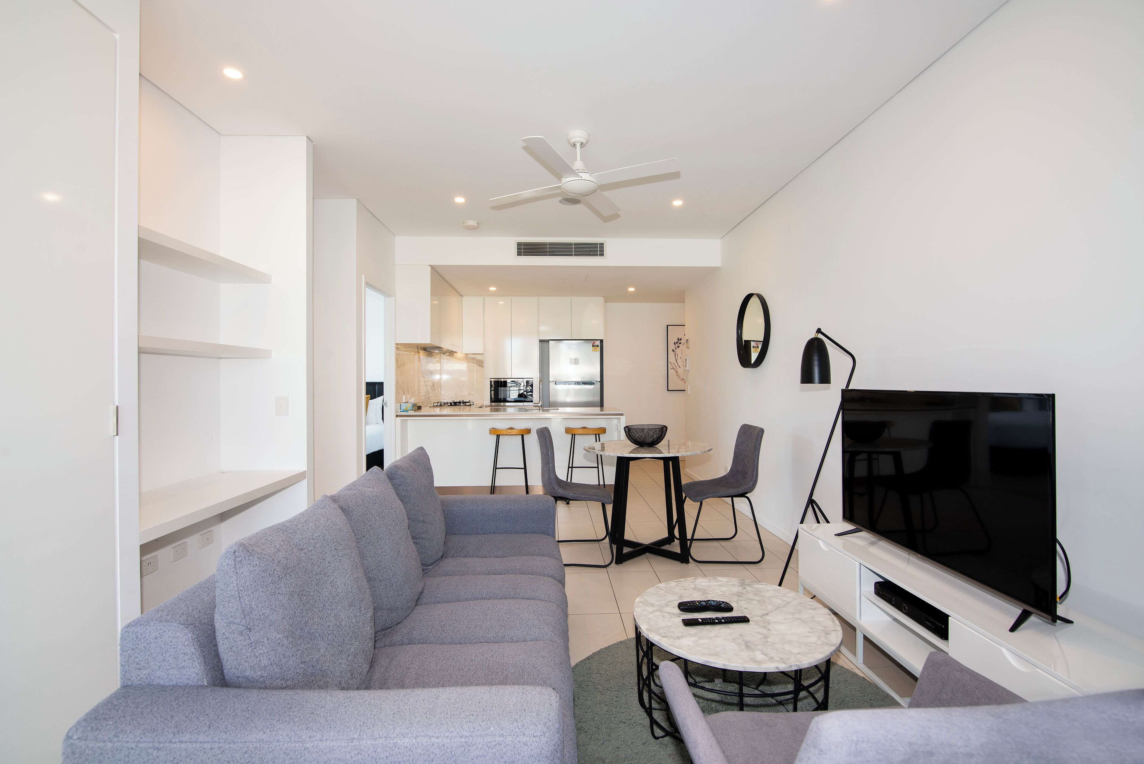 A modern living room with a grey sofa, a TV, and a dining area with a table and chairs.