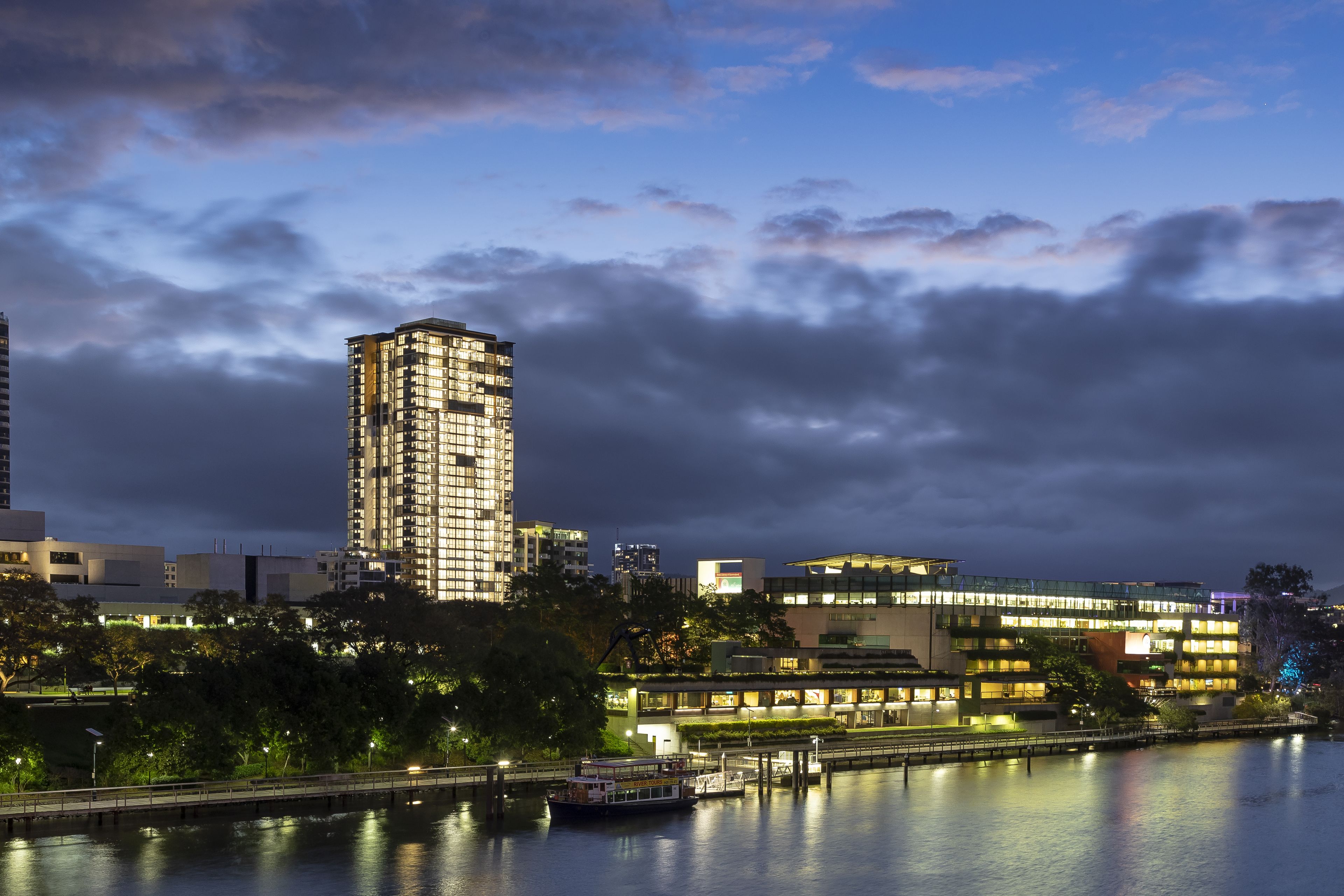 A high-rise building with multiple floors, a waterfront view, and a bridge in the foreground.