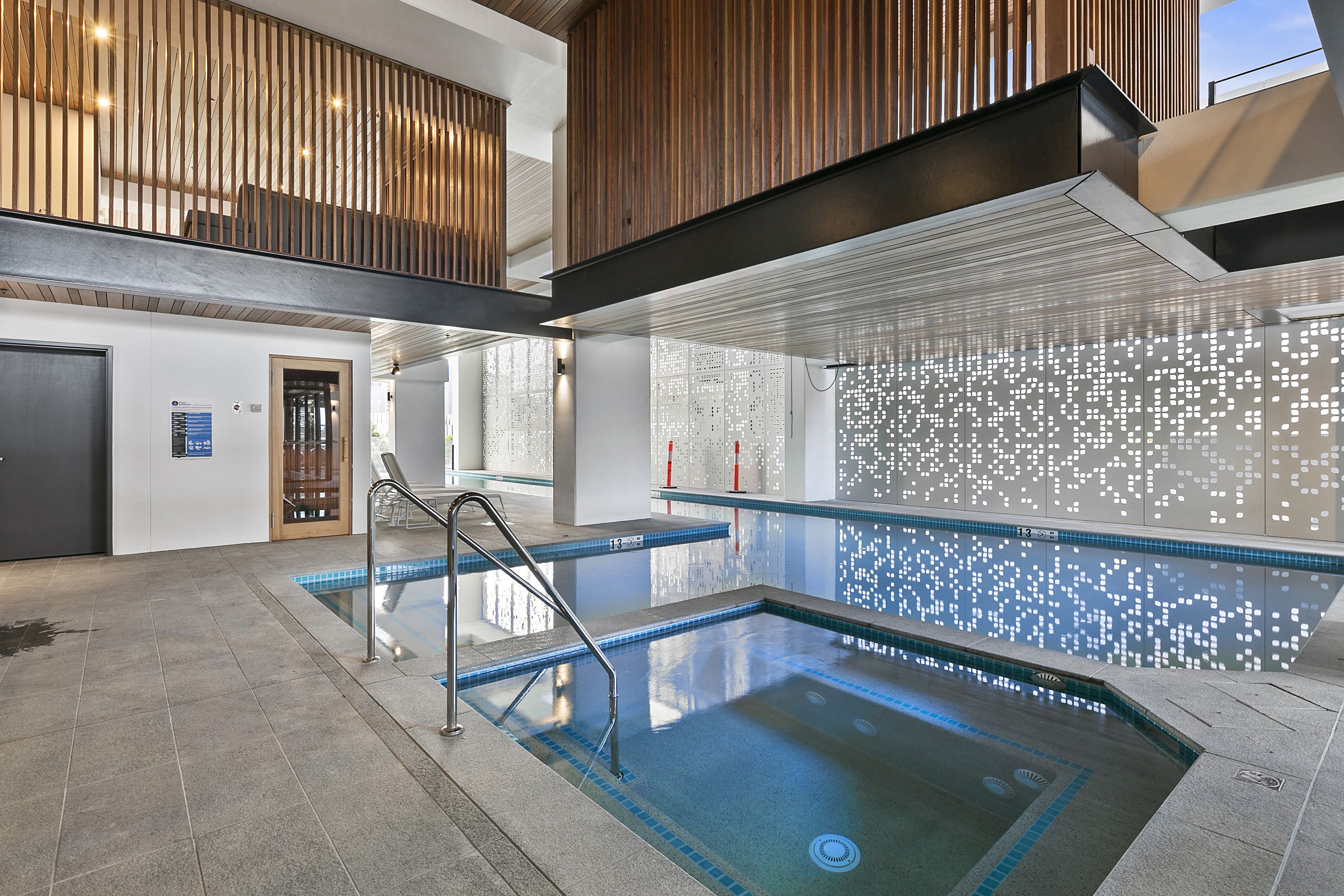 A modern indoor swimming pool with clear water, a wooden ceiling, and a decorative light wall.