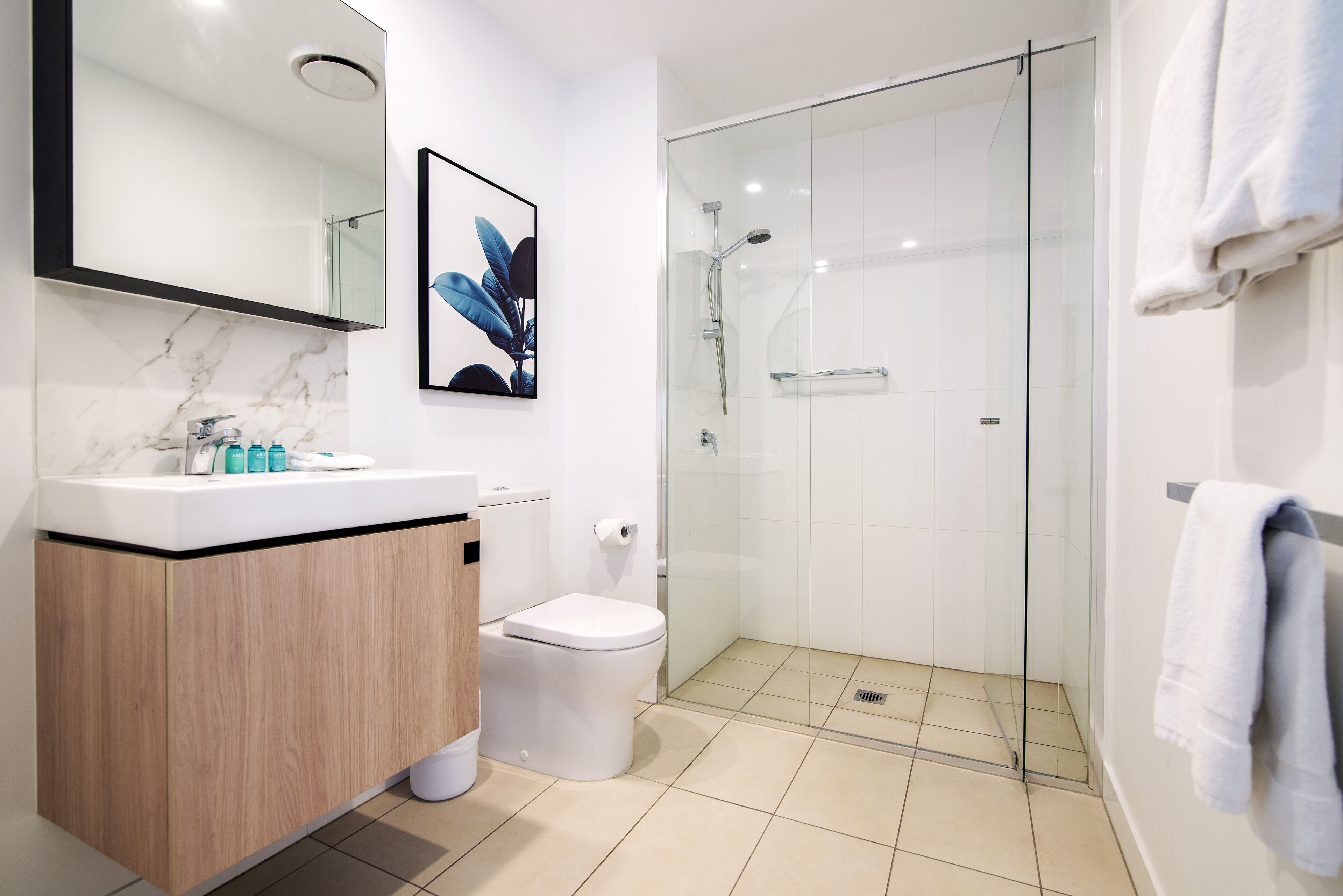 A modern bathroom with a marble sink, a toilet, a glass shower enclosure, and a large mirror.