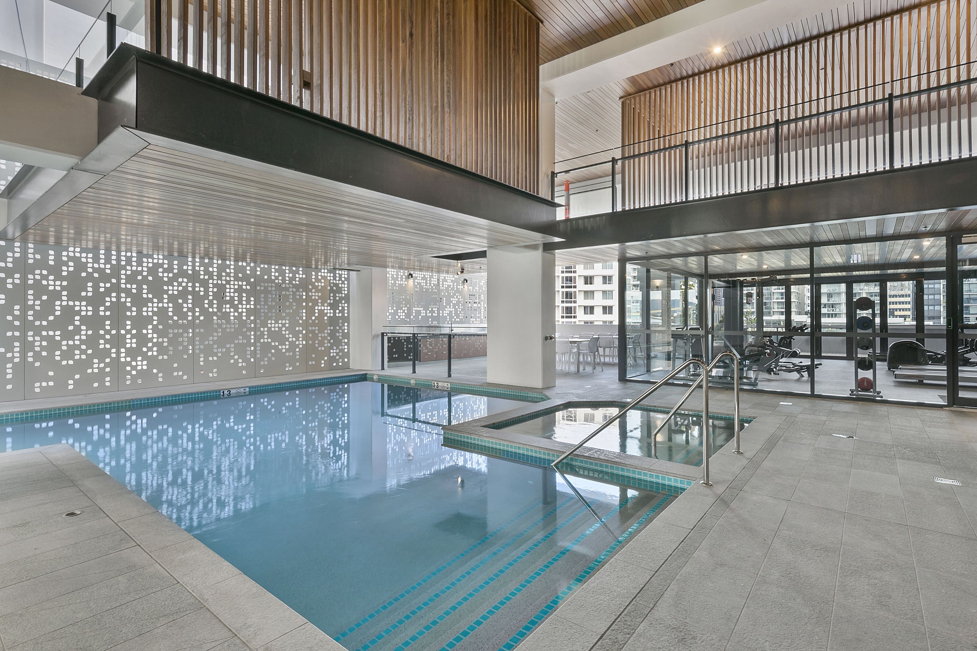 Una piscina interna moderna con acqua cristallina, immersa in un'ampia area caratterizzata da soffitto alto e rivestimenti in legno.