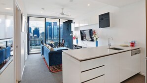 Een moderne keuken met een groot eiland, een zithoek met een blauwe bank en een stadszicht door grote ramen.