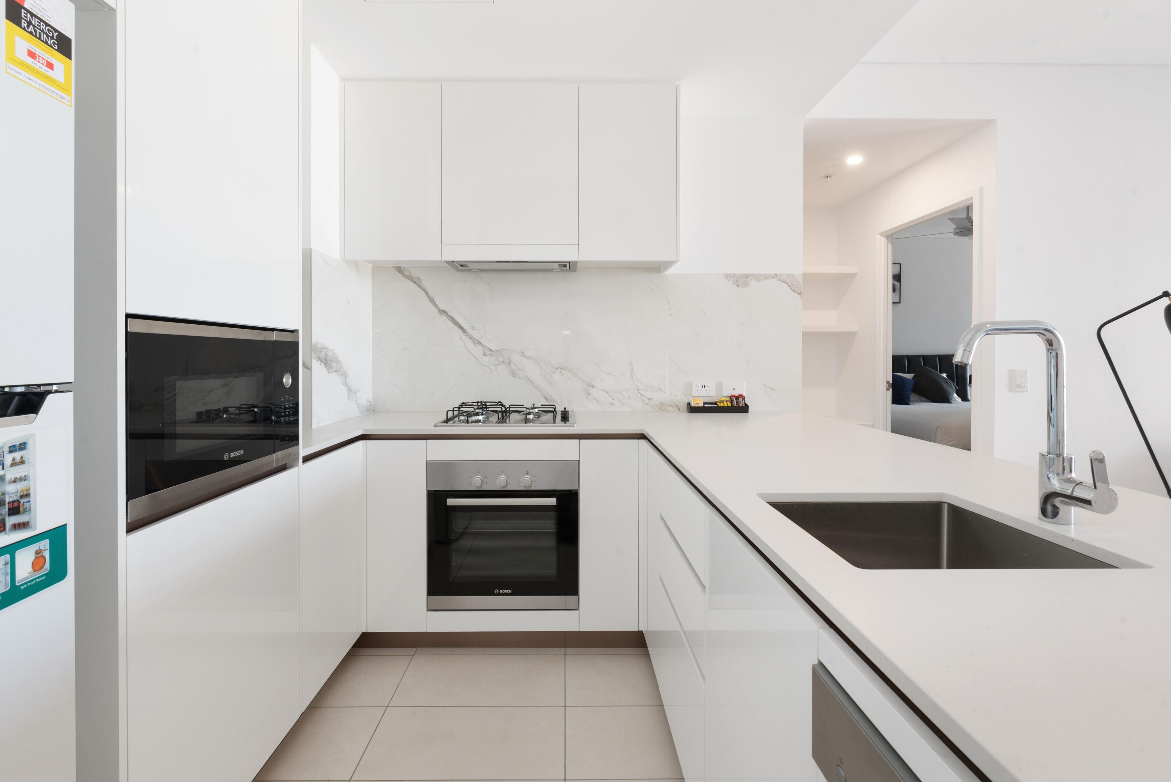 A modern kitchen with white cabinetry, a built-in oven, a gas stove, and a sink.