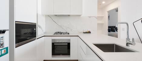 A modern kitchen with white cabinetry, a built-in oven, a gas stove, and a sink.