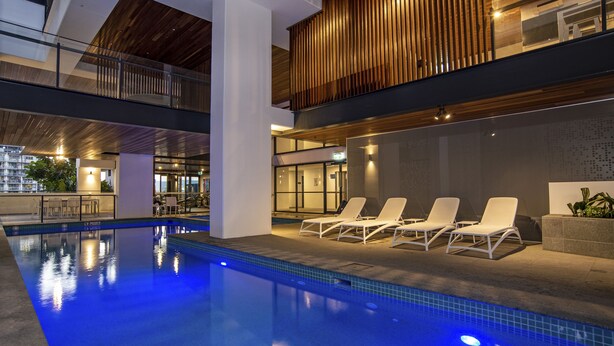 Een modern zwembad binnen met lounge stoelen en een glazen balustrade.