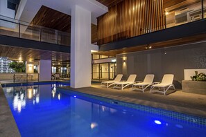 Uma área interna de piscina moderna, com espreguiçadeiras e guarda-corpo de vidro.