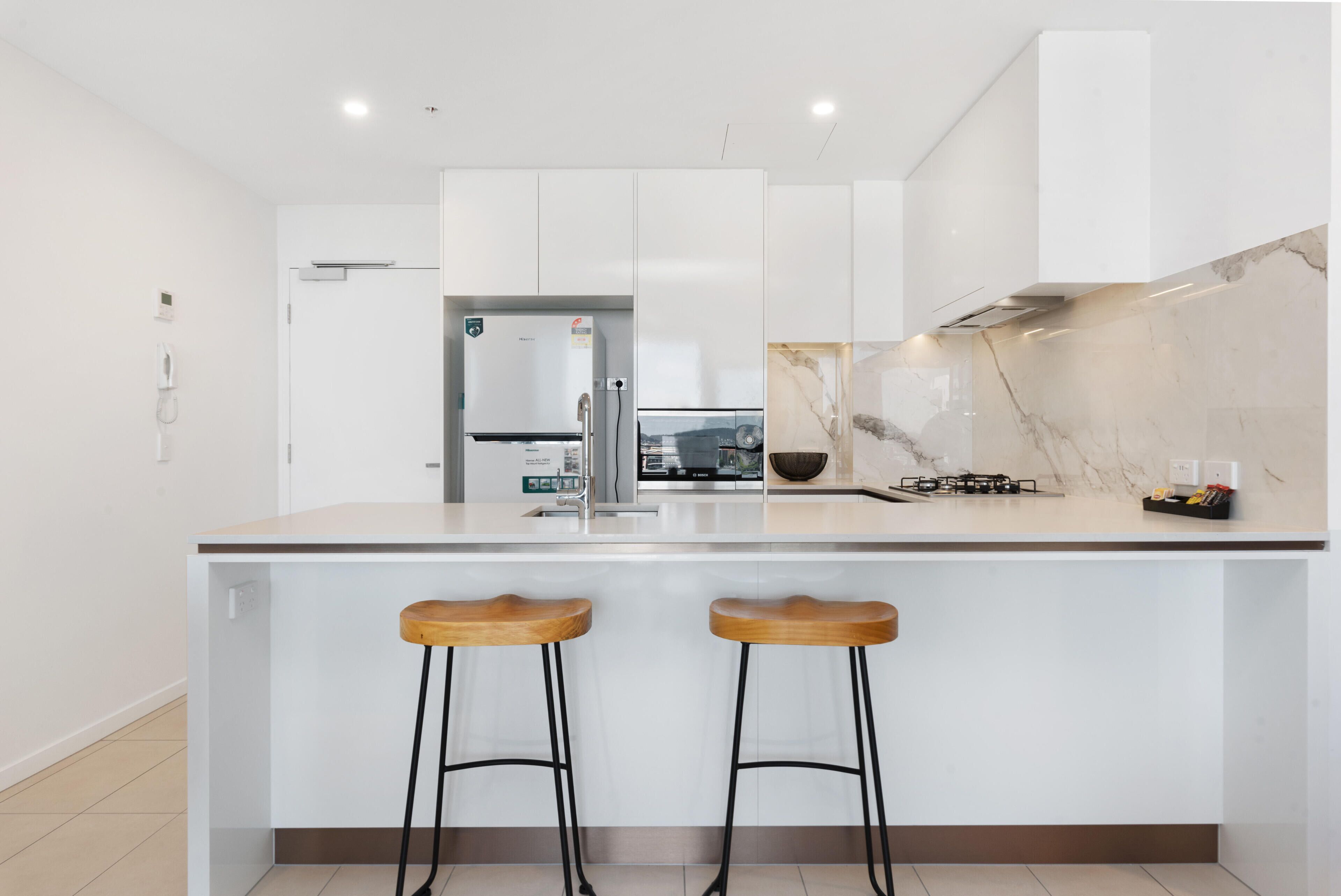 A modern kitchen with white cabinets, a marble backsplash, and two wooden stools.