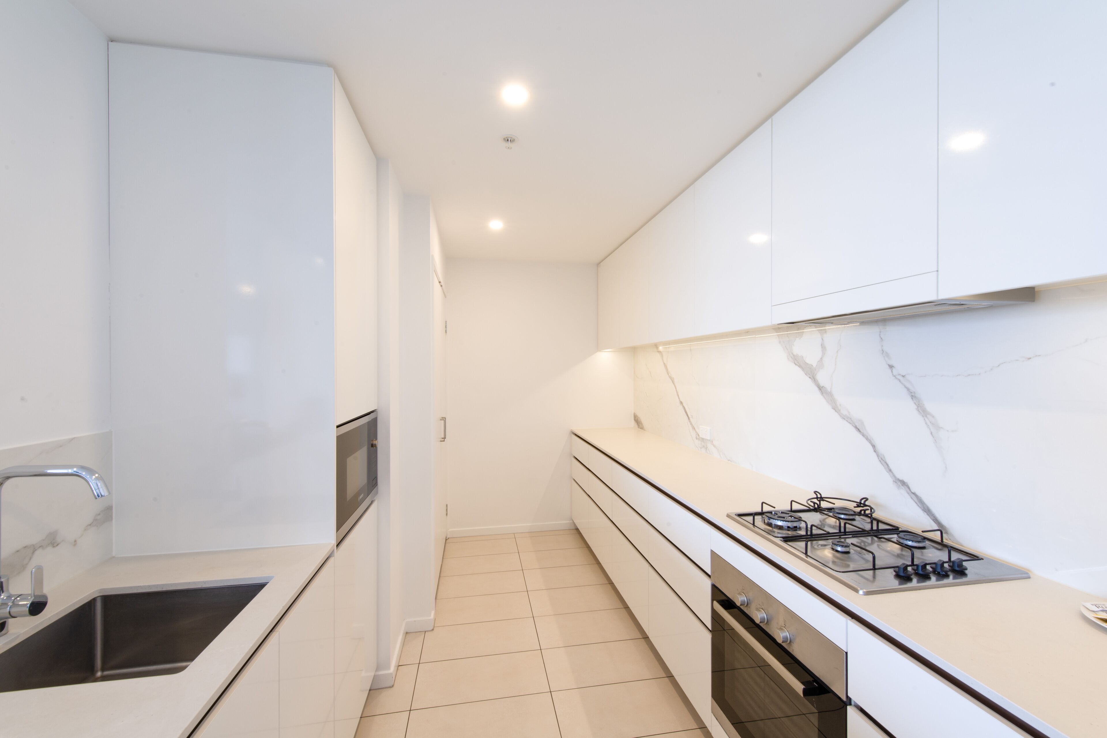 A modern kitchen with white cabinetry, a stainless steel sink, a gas stove, and a marble backsplash.