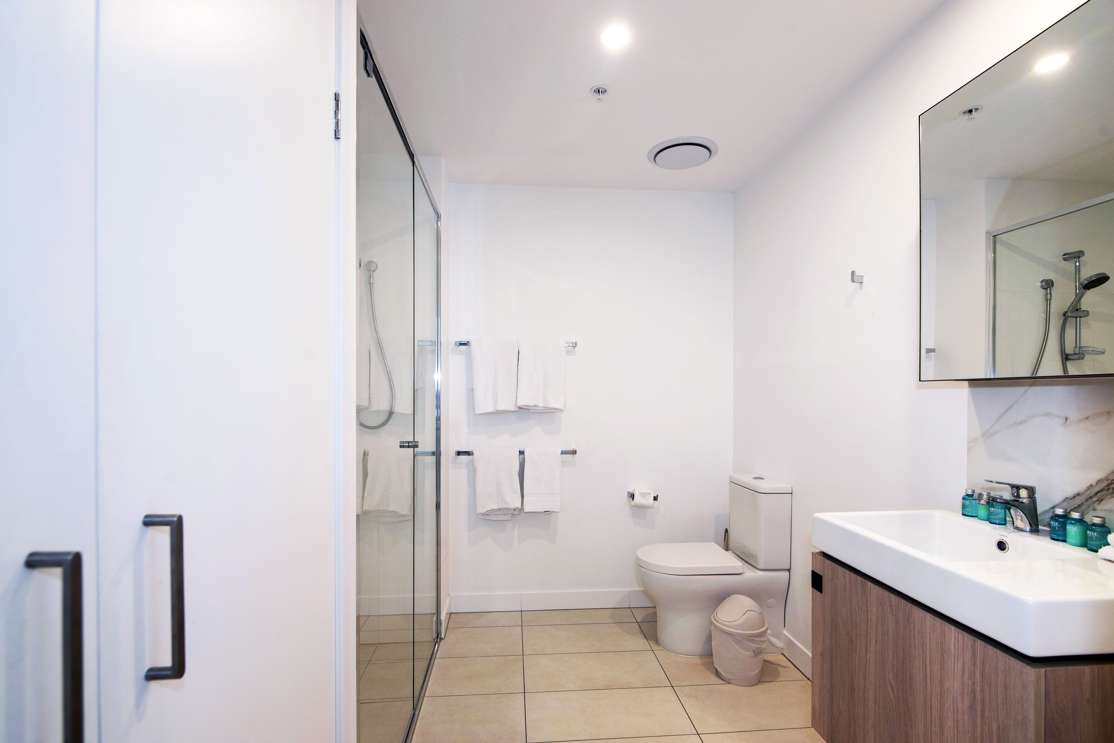 Een moderne badkamer met een douchecabine van glas, een toilet, een wastafel met een marmeren aanrechtblad en een spiegel boven de wastafel.