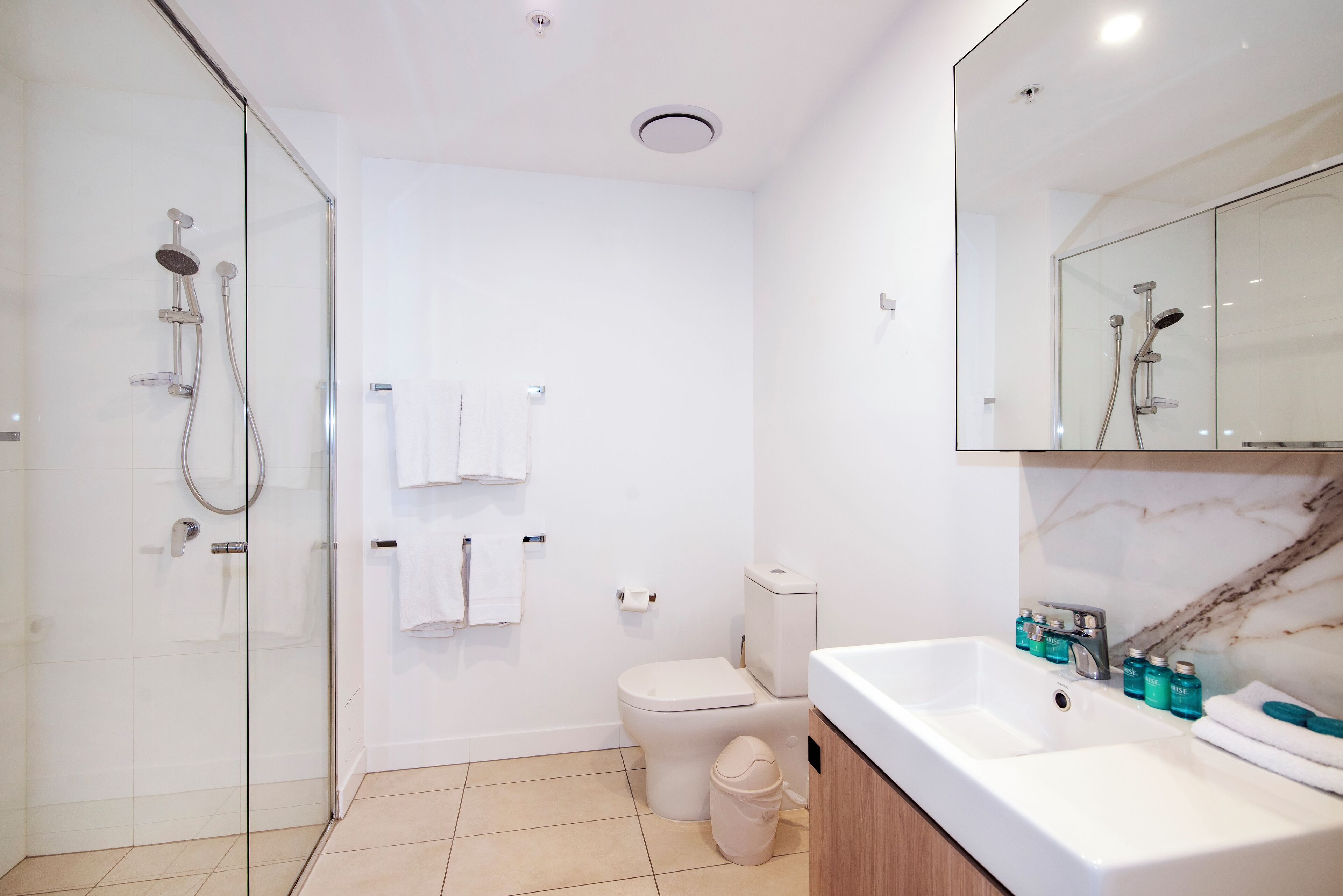 A modern bathroom with a glass-enclosed shower, a toilet, and a sink with toiletries.