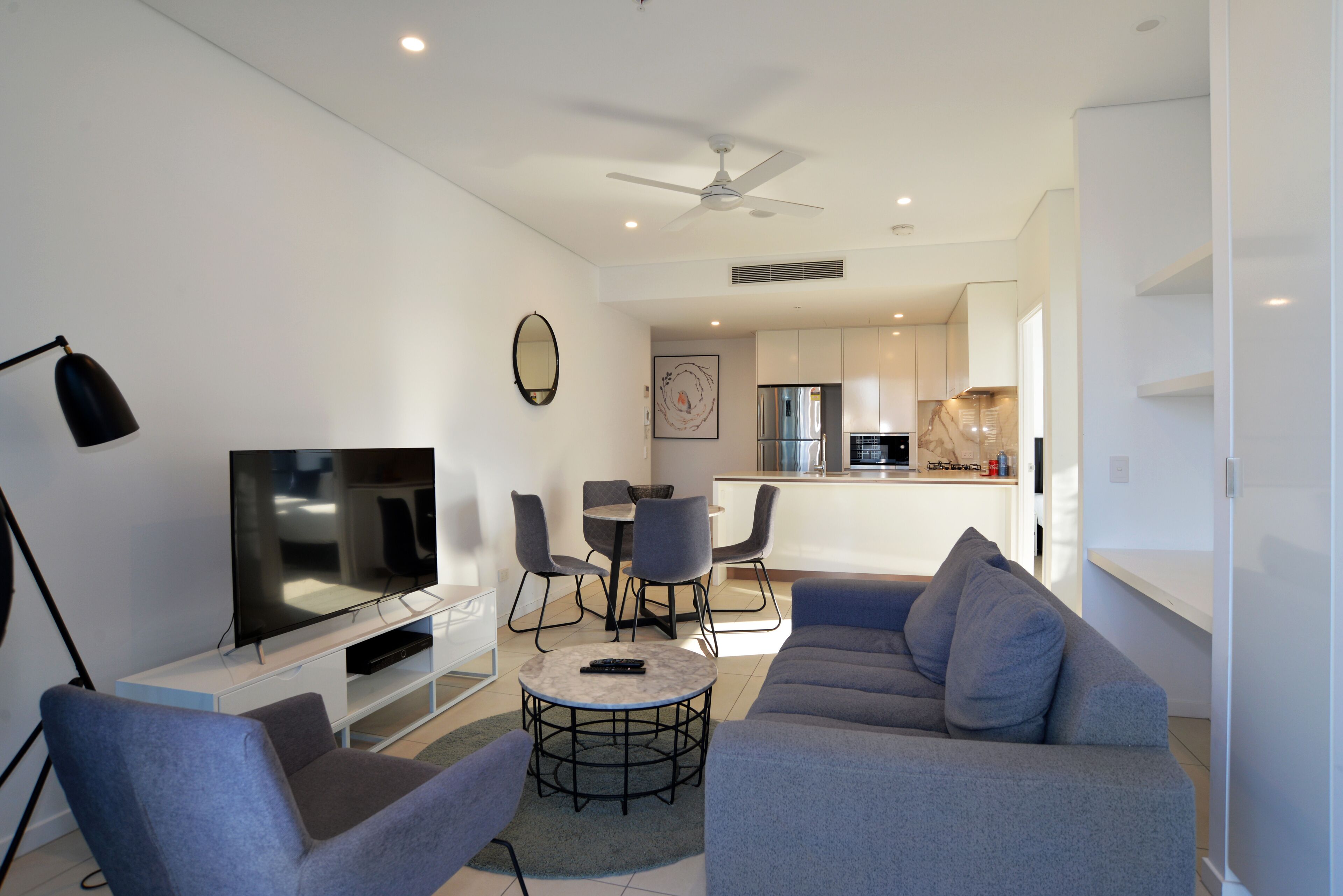 A modern living room with a grey sofa, a TV, and a dining area with chairs and a table.