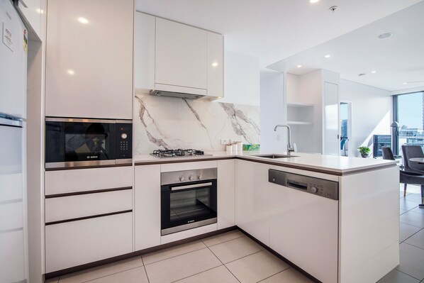 Cozinha moderna com micro-ondas, forno e lava-louças Bosch, armários brancos e painel de fundo em mármore.