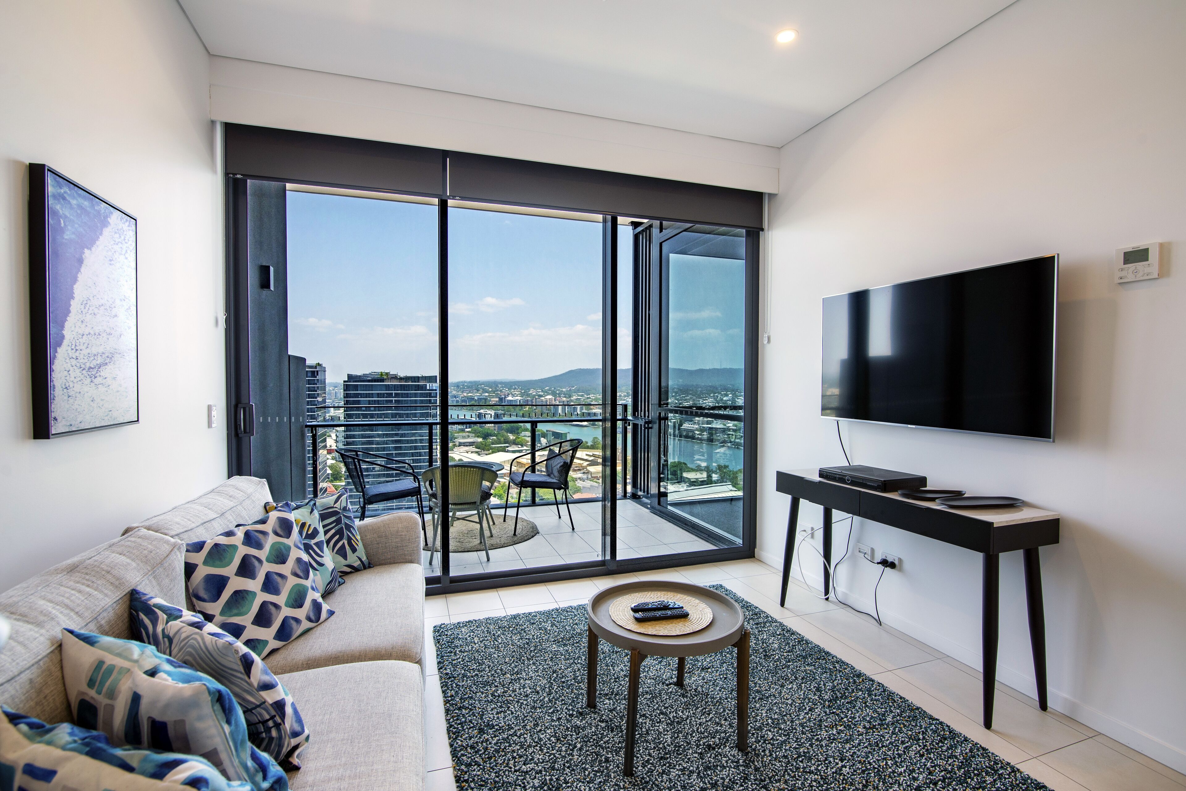 A modern living room with a sofa, a coffee table, a TV, and a balcony with a view of the city.